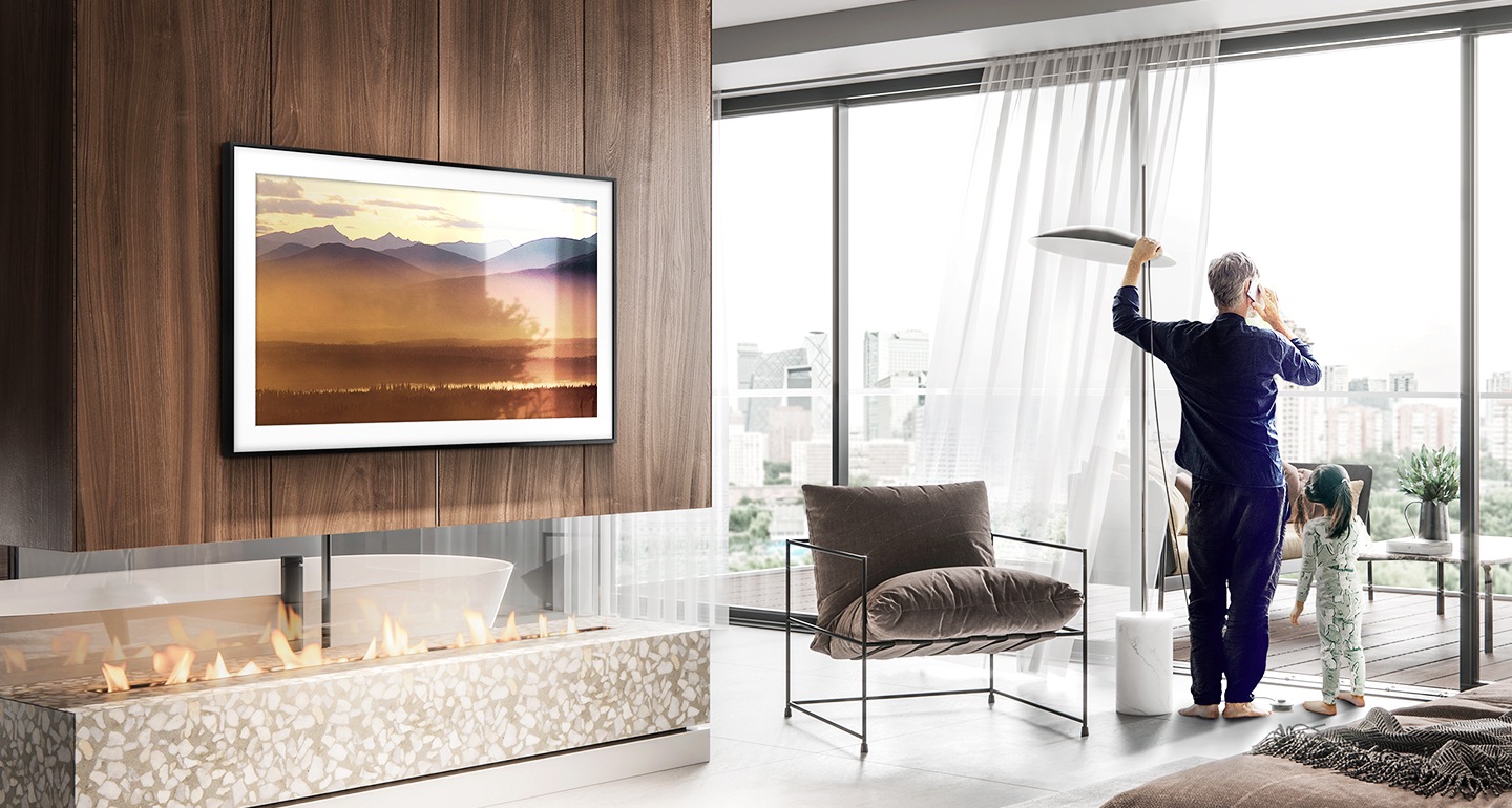 A man and child stand in the living room looking out onto the terrace. Samsung’s The Frame displays a beautiful mountain landscape on screen.