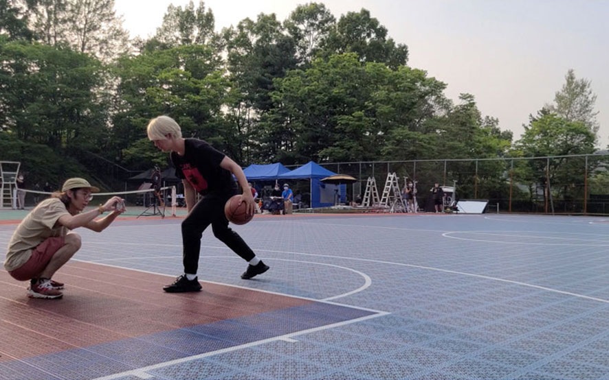 A crew member filming an actor dribbling a basketball on a basketball court.