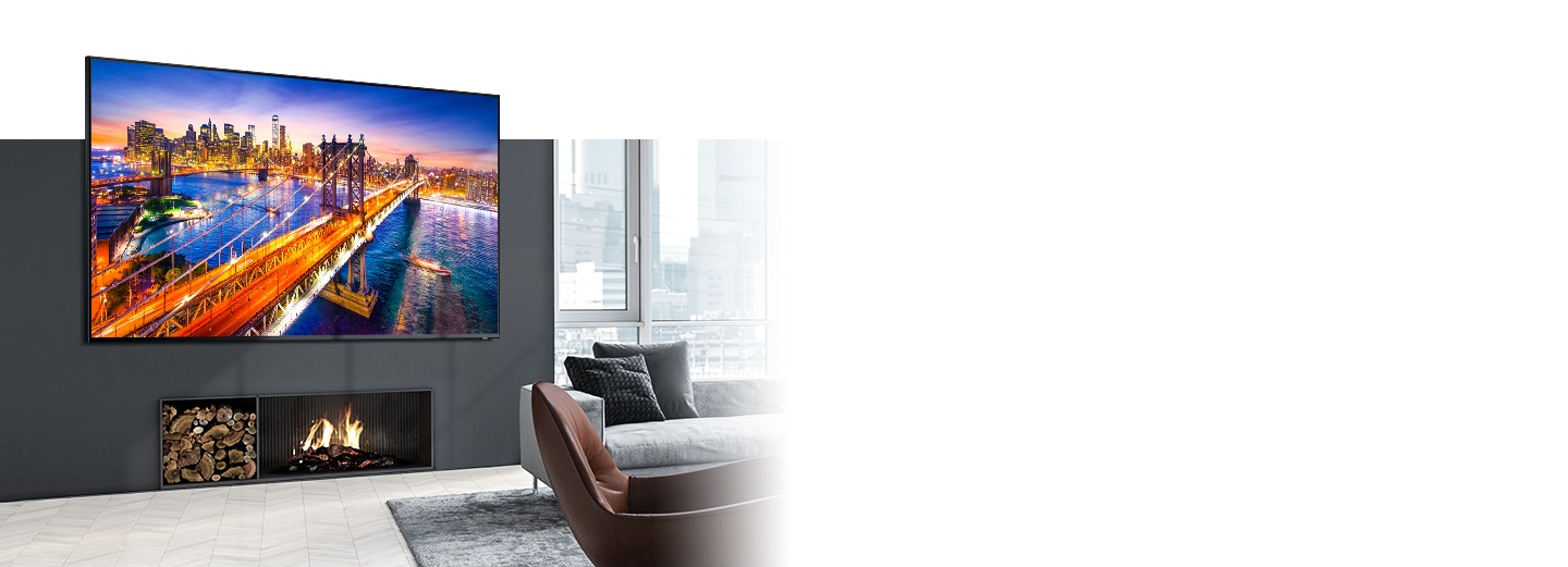 Un téléviseur mural au-dessus d’une cheminée affiche un pont de nuit avec une ville en qualité d’image claire grâce aux paramètres d’image Samsung du Mode Dynamique dans le salon lumineux et confortable.