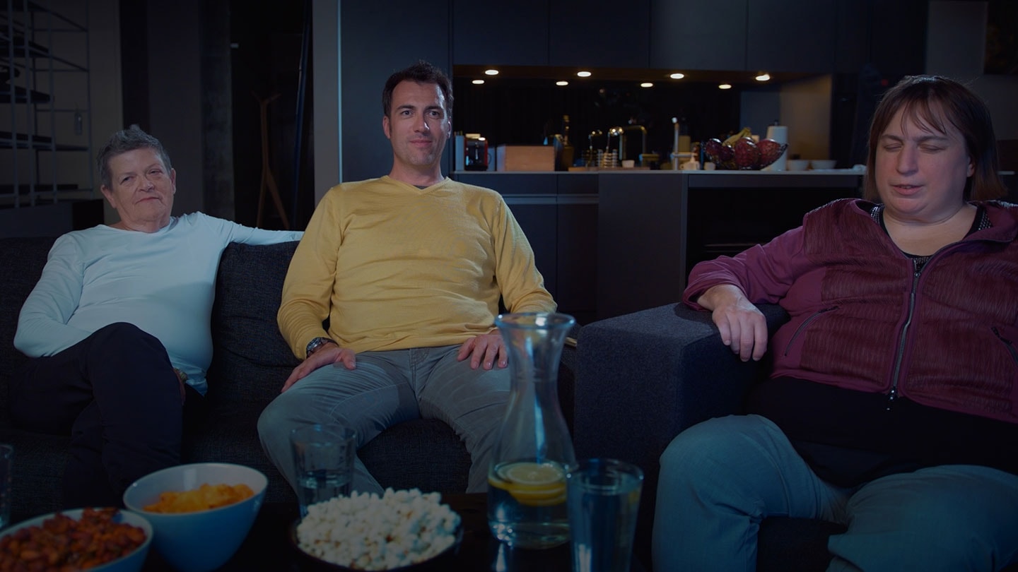 L'image montre un groupe de trois personnes lors d'une soirée télévisée en autocar dans un salon.
