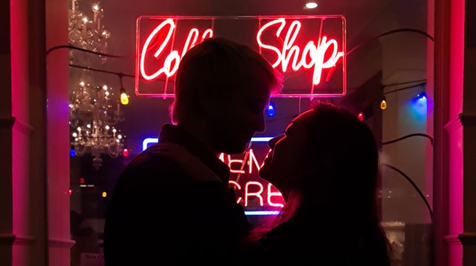 Schattenfoto eines Pärchens vor der Neonbeleuchtung eines Cafés. Die Kulisse ist dunkel, aber ihre Silhouette ist erkennbar