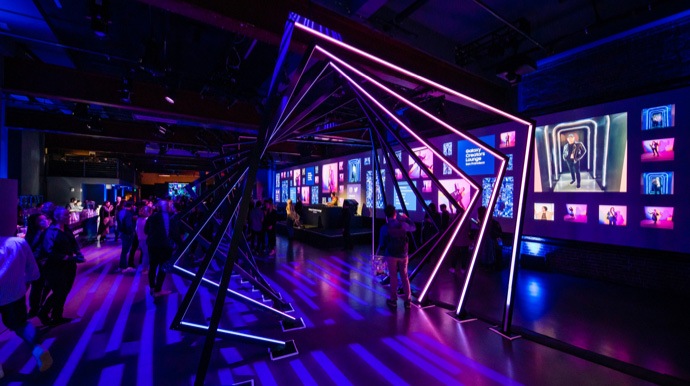 Influencer versammelt im Creators Lounge Event Space. Man sieht die farbenfrohe Lichtinstallation vorn und eine DJ-Bühne und Bar im Hintergrund.