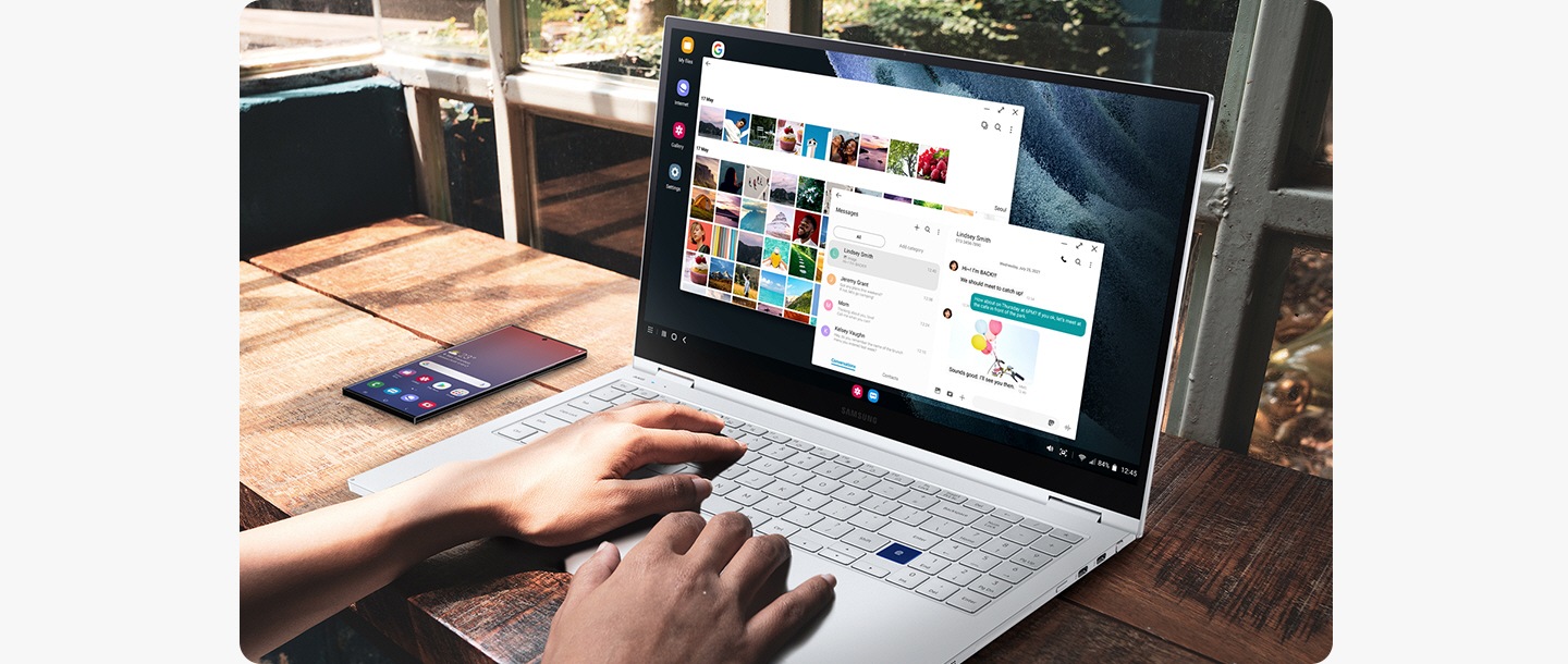 Un usuario utiliza una computadora portátil Samsung. Junto a la computadora, hay un teléfono inteligente Galaxy que muestra la pantalla de inicio. Con DeX, el usuario utiliza la pantalla de la computadora portátil para ver la galería mientras envía mensajes de texto.