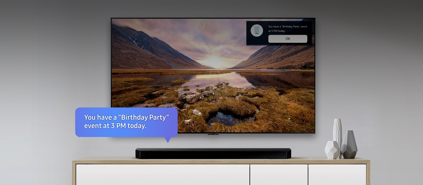 Un televisor Samsung en el centro y una barra de sonido ubicada debajo. Hay una burbuja de texto azul en la barra de sonido que dice: “Hoy tienes el evento Fiesta de cumpleaños a las 3:00 p. m.”. En la esquina superior derecha del televisor, aparece una notificación con el mismo recordatorio y el botón “Aceptar”.