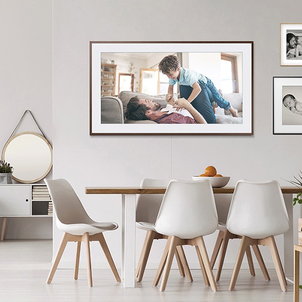 Televisor The Frame que muestra una fotografía familiar colgado sobre la pared de una sala con una mesa y cinco sillas.