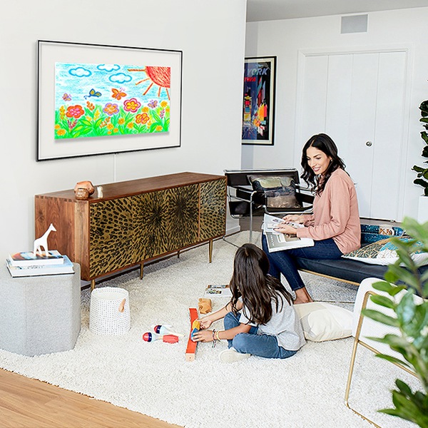 Una madre y su hija se encuentran conversando en la sala de estar mientras un televisor The Frame colgado en la pared muestra las obras de arte de las niñas.