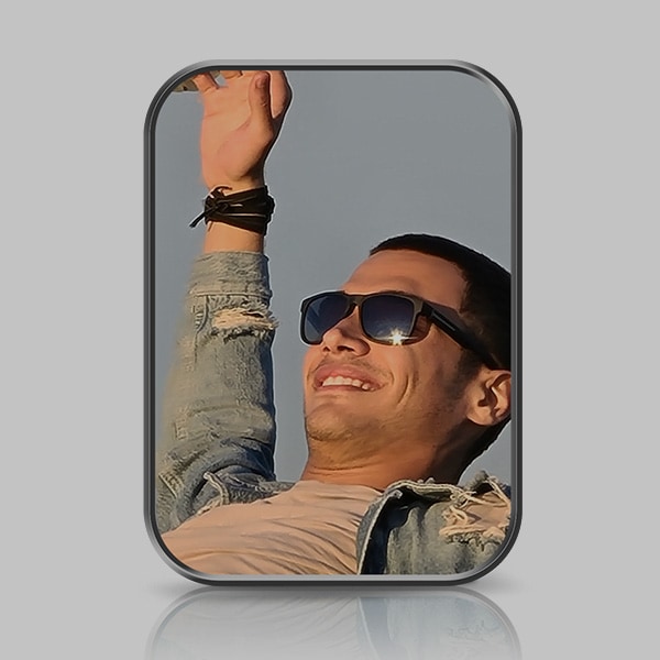 Un plano de un hombre sonriendo con gafas y el brazo derecho levantado y extendido hacia el cielo.