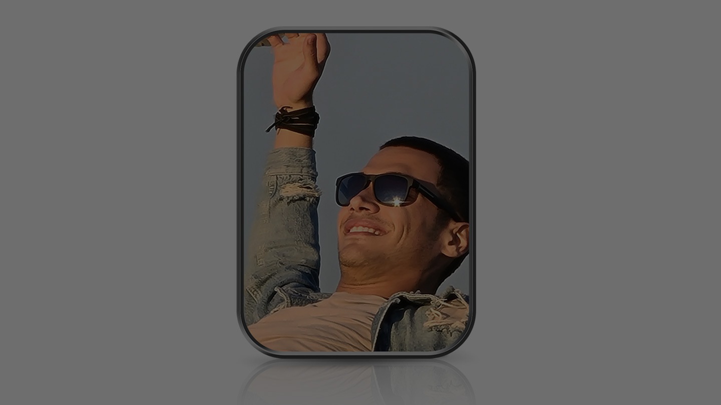 Un plano de un hombre sonriendo con gafas y el brazo derecho levantado y extendido hacia el cielo.