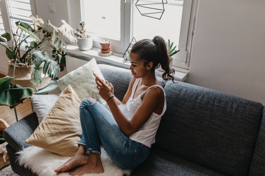 Una señora está sentada en un sofá en una habitación llena de plantas y está hablando por teléfono