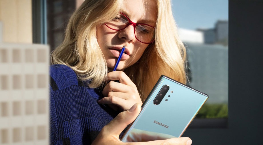 Una mujer sosteniendo un S Pen en sus labios mientras mira su teléfono Galaxy Note10