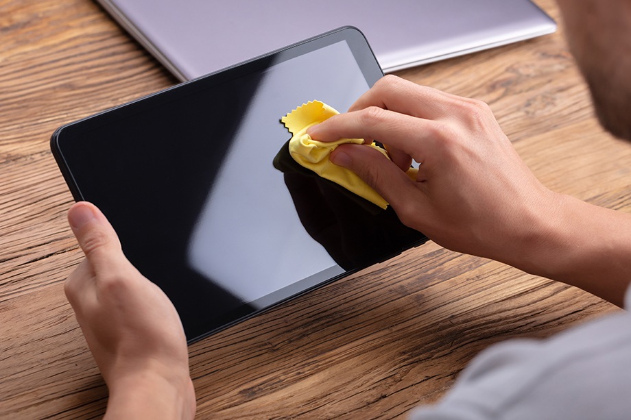 La mano de un hombre limpiando la pantalla de su tableta digital con un paño amarillo suave