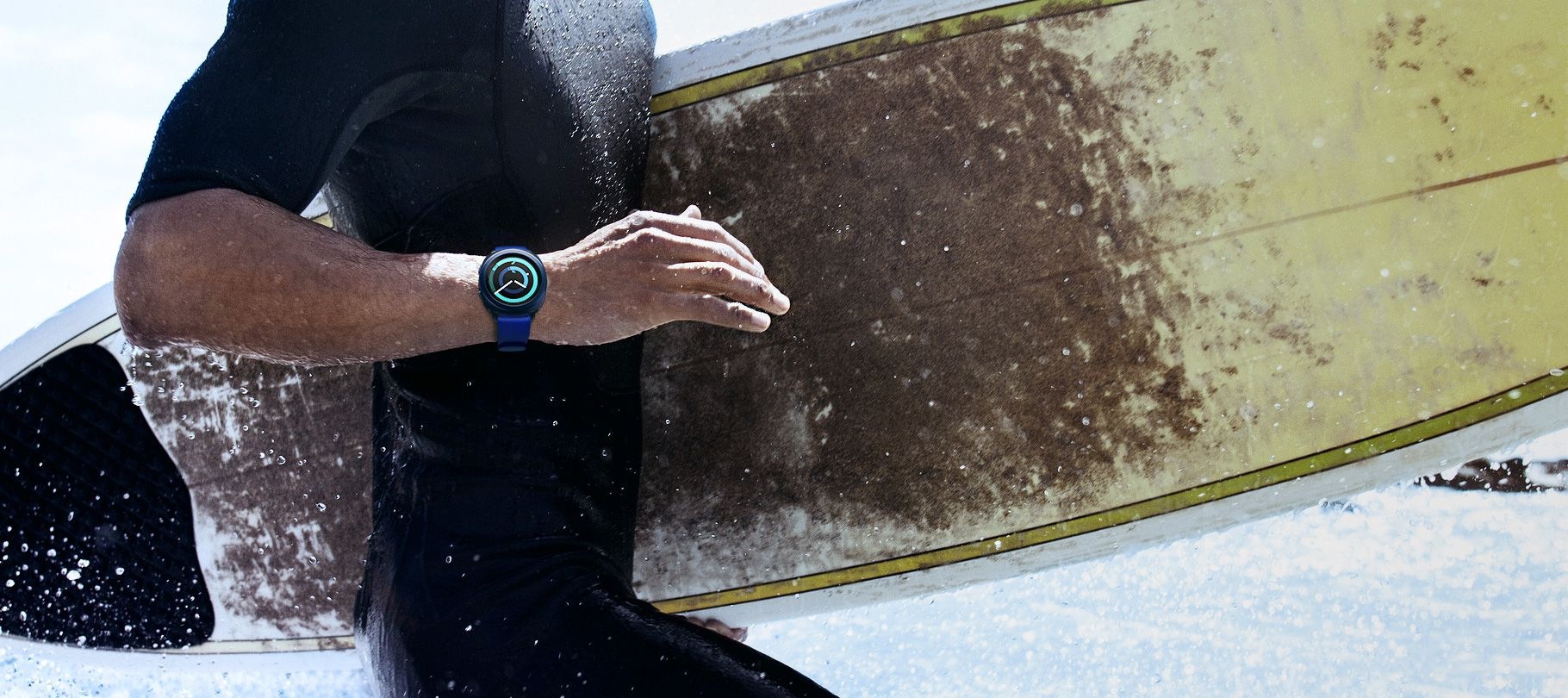 Image of man carrying a surfboard with Gear Sport in blue on his wrist