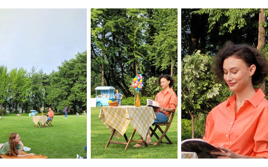 امرأة ترتدي قميصًا برتقاليًا تجلس على طاولة تنزه في حديقة خضراء، وتقرأ كتابًا. يتم تكبير المشهد حتى 10 أضعاف و100 ضعف في اللقطات المقابلة. 