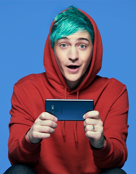 A photo of  the gamer Ninja against a blue background holding a prism black Samsung Galaxy S10