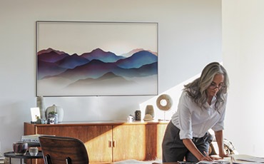 A lifestyle image of the 2018 new QLED TV Q9F. Image shows QLED TV is mounted on wall with Ambient Mode in a sunny room, and a woman is working naturally.