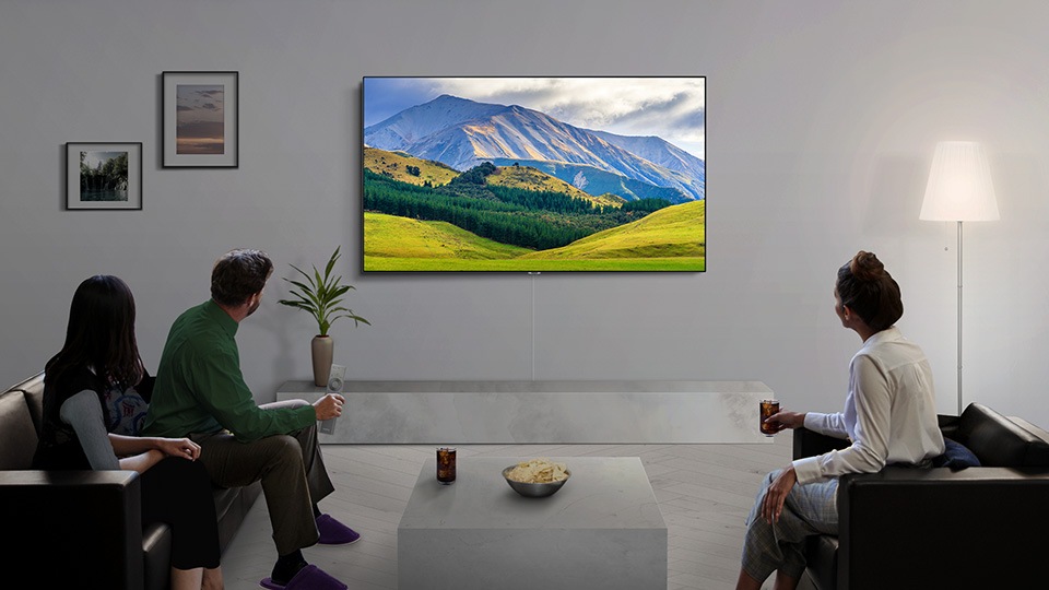 Three people sitting in a living room and watching Samsung’s QLED TV together