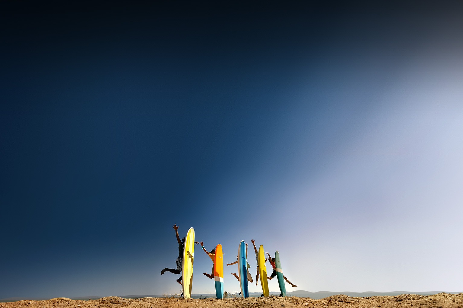 A photo taken by Galaxy S8 or S8+ of young people jumping in the air behind their surfboards stuck standing up in the sand