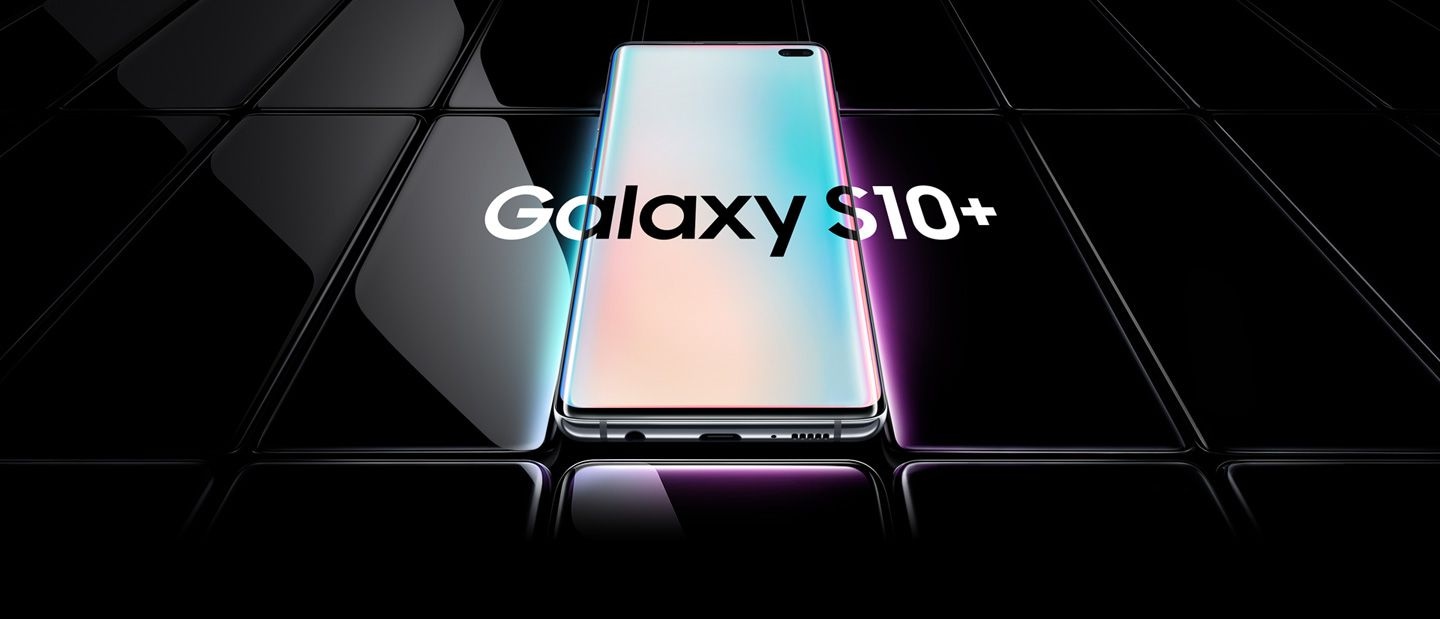 Several Galaxy S10 plus phones all laid flat and seen at an angle. All are black except the one in the middle, which is shown with a prismatic gradient onscreen with Galaxy S10 plus overlaid on top of it and the two phones on either side.