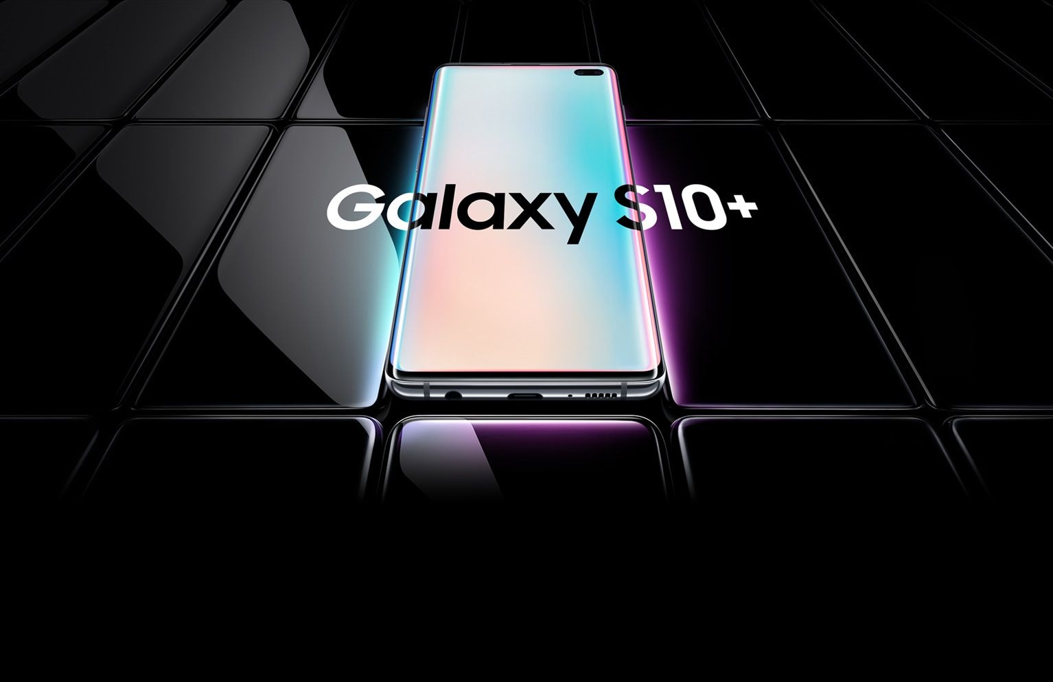 Several Galaxy S10 plus phones all laid flat and seen at an angle. All are black except the one in the middle, which is shown with a prismatic gradient onscreen with Galaxy S10 plus overlaid on top of it and the two phones on either side.