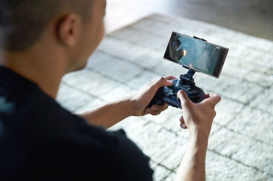 عکسی از بالای شانه اسطوره که او را درحال بازی روی تلفن Galaxy Note20 خودش نشان می‌دهد درحالی‌که آن را در یک دسته بازی مخصوص Xbox Game Pass Ultimate قرار داده است.