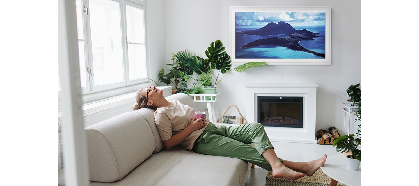 یک زن روی کاناپه خود دراز کشیده است در حالی که تصویری هوایی از بورا بورا روی The Frame نمایش داده می‌شود.