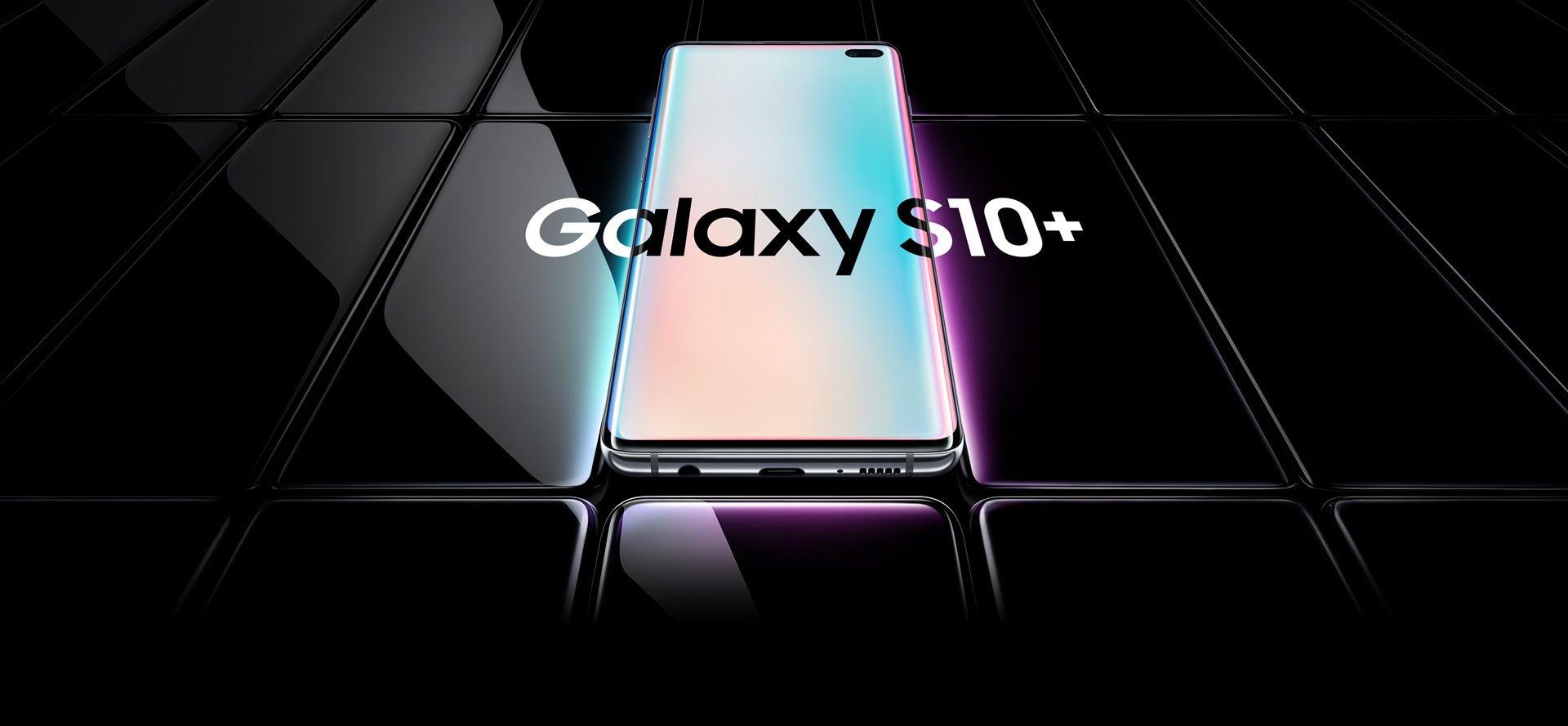 Several Galaxy S10 plus phones all laid flat and seen at an angle. All are black except the one in the middle, which is shown with a prismatic gradient onscreen with Galaxy S10 plus overlaid on top of it and the two phones on either side.