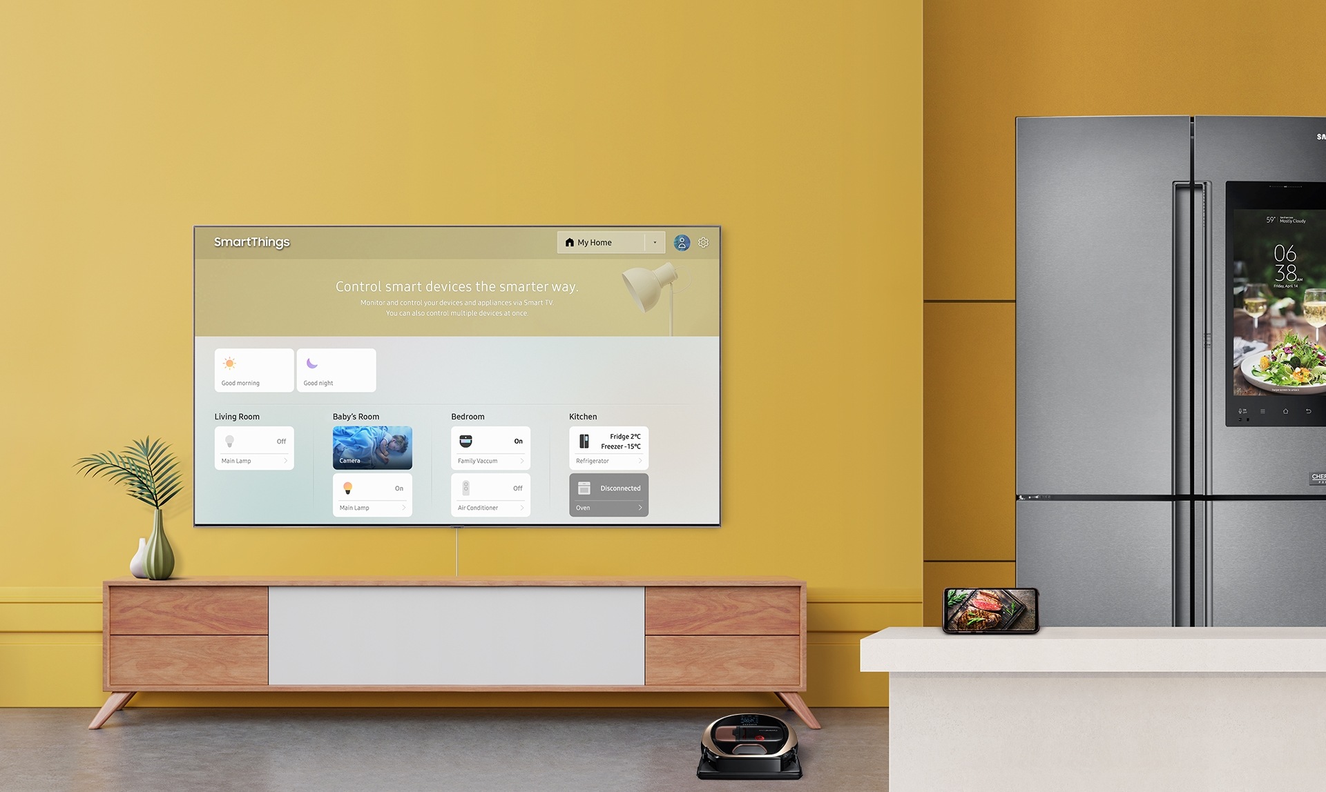 Un televisor Samsung QLED de 2019 que muestra un panel de SmartThings en un televisor inteligente montado en una pared rodeado por dispositivos y aparatos domésticos conectados de muestra: un refrigerador, un teléfono inteligente y una aspiradora.