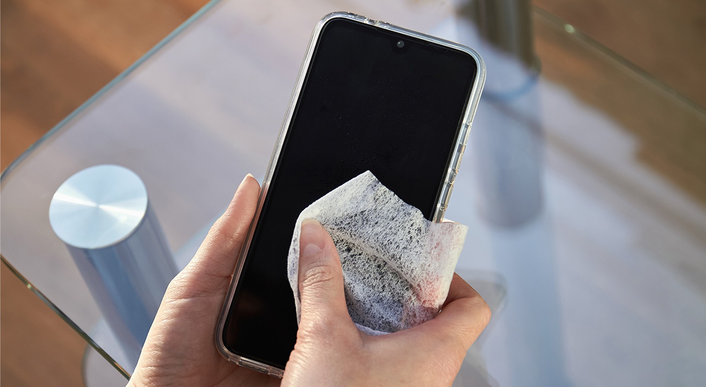 Woman's hands wipe smartphone screen with disinfectant cloth. Close-up woman cleans her mobile phone standing on city street.