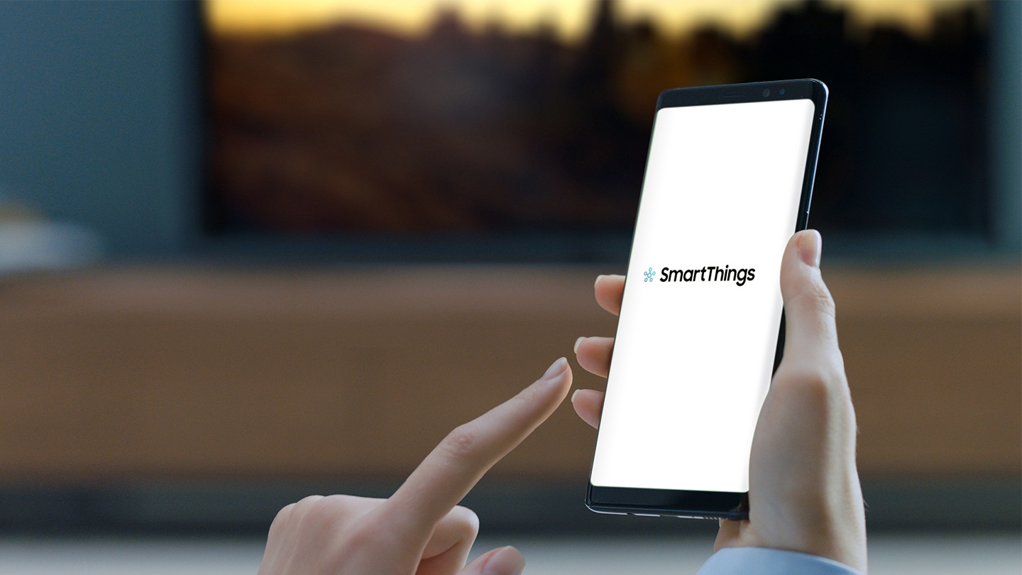 يشير الإصبع إلى هاتف محمول. تعرض شاشة الهاتف المحمول تطبيق SmartThings.