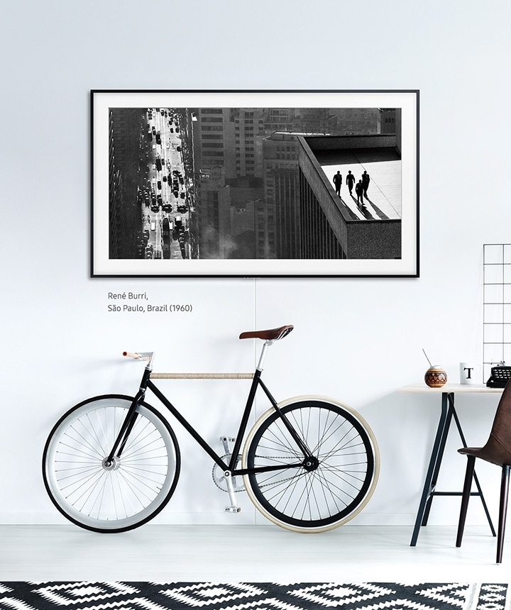 The Frame hanging on a wall above a bicycle and desk with the basic charcoal black frame.