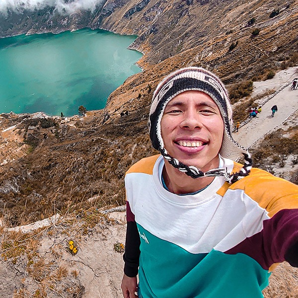 Un homme souriant portant un bonnet péruvien fait un selfie avec en contrebas un lac