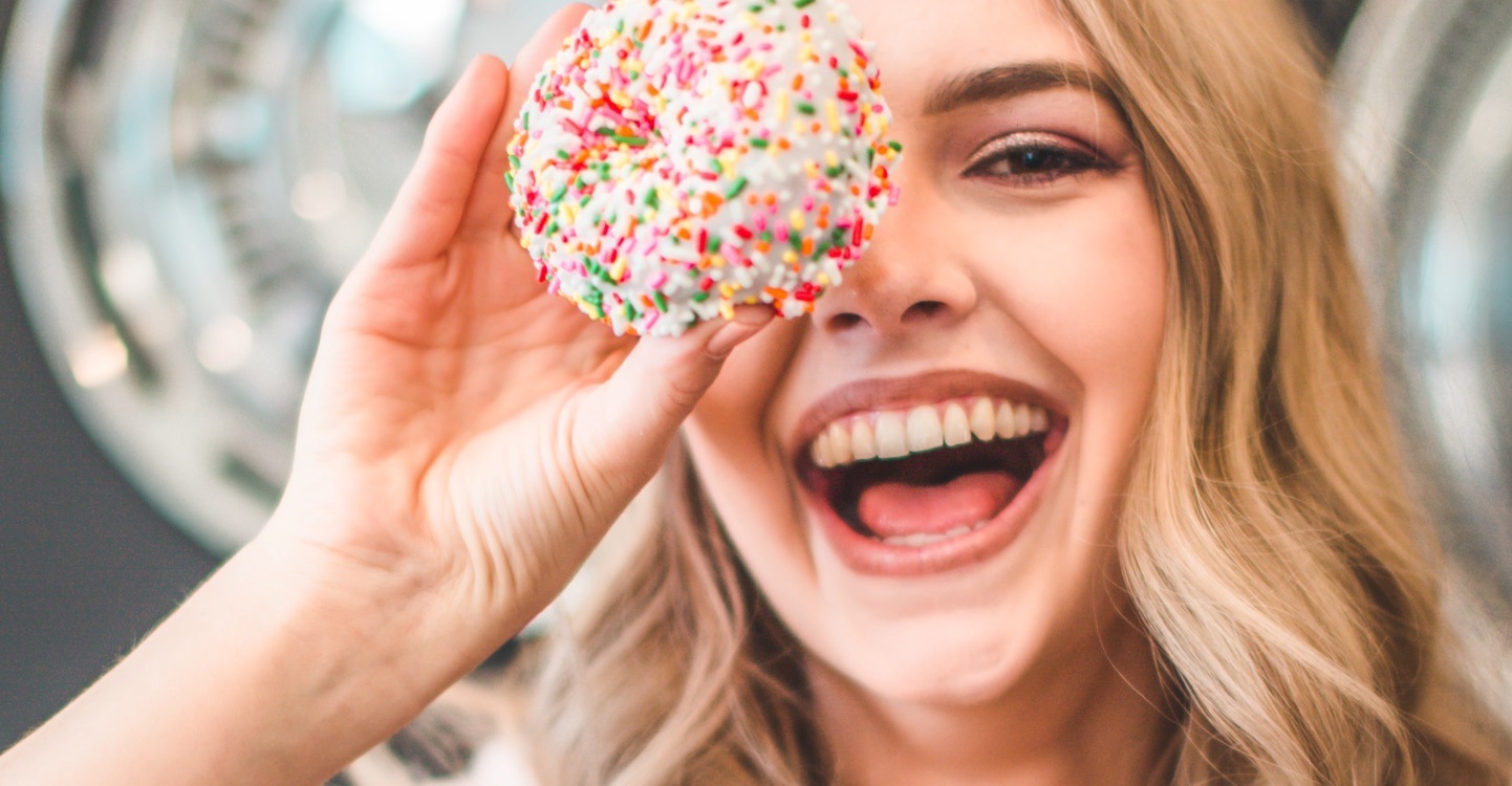 Een vrouw kijkt lachend in de camera met een donut in haar hand gemaakt met een Samsung combimagnetron AirFry functie.