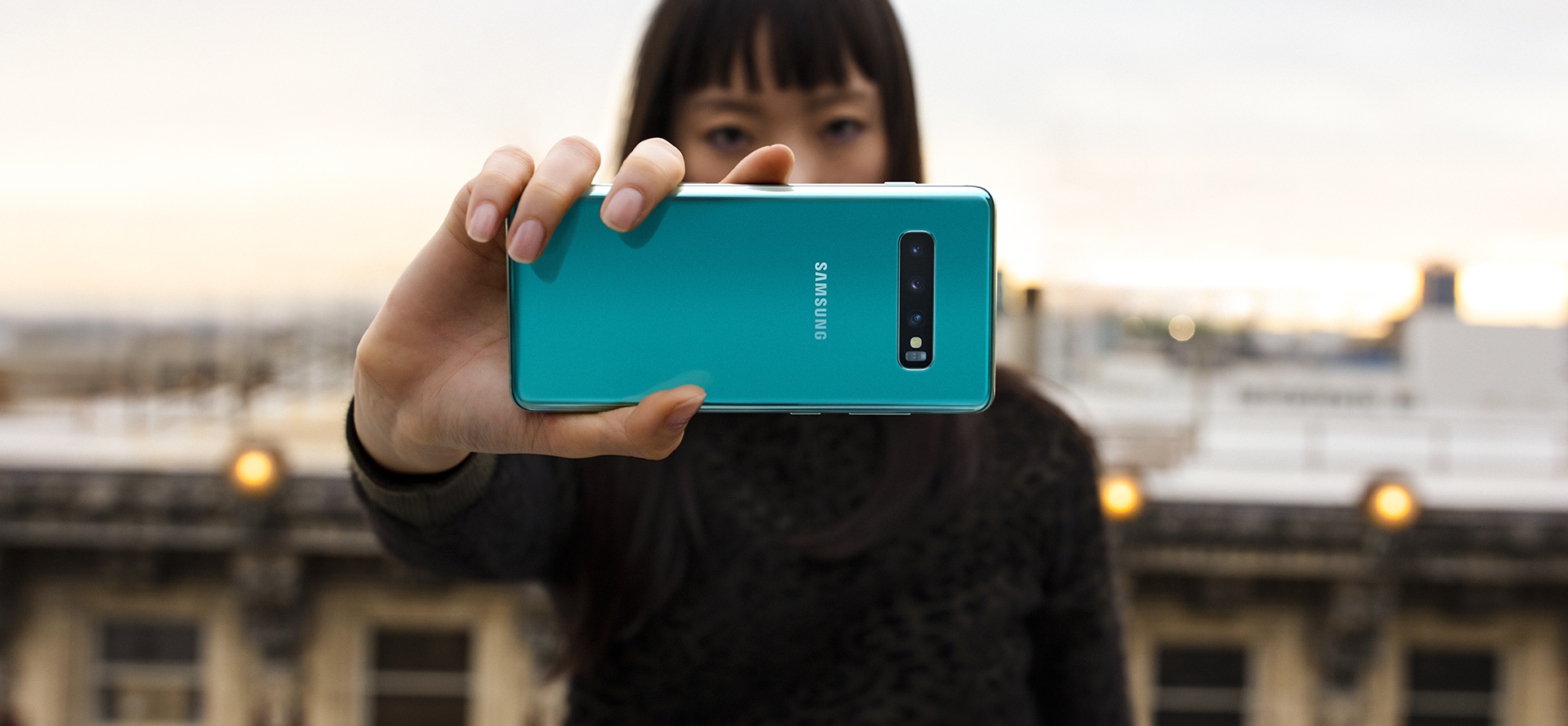 A woman holding Galaxy S10 plus in Prism Green to show the Pro-grade three camera system.