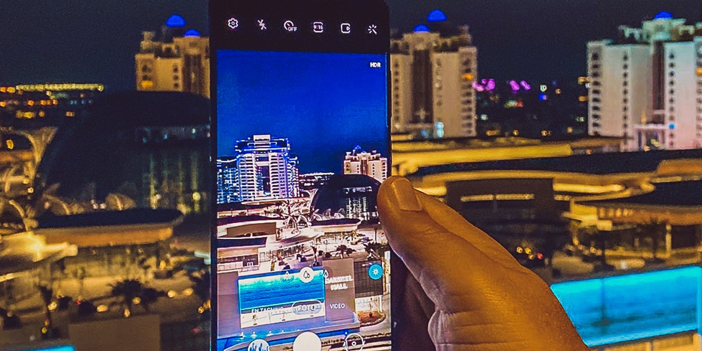 Billede af mobilen Samsung Galaxy S20, mens den anvendes til at fotografere udsigten ud over en by om natten.