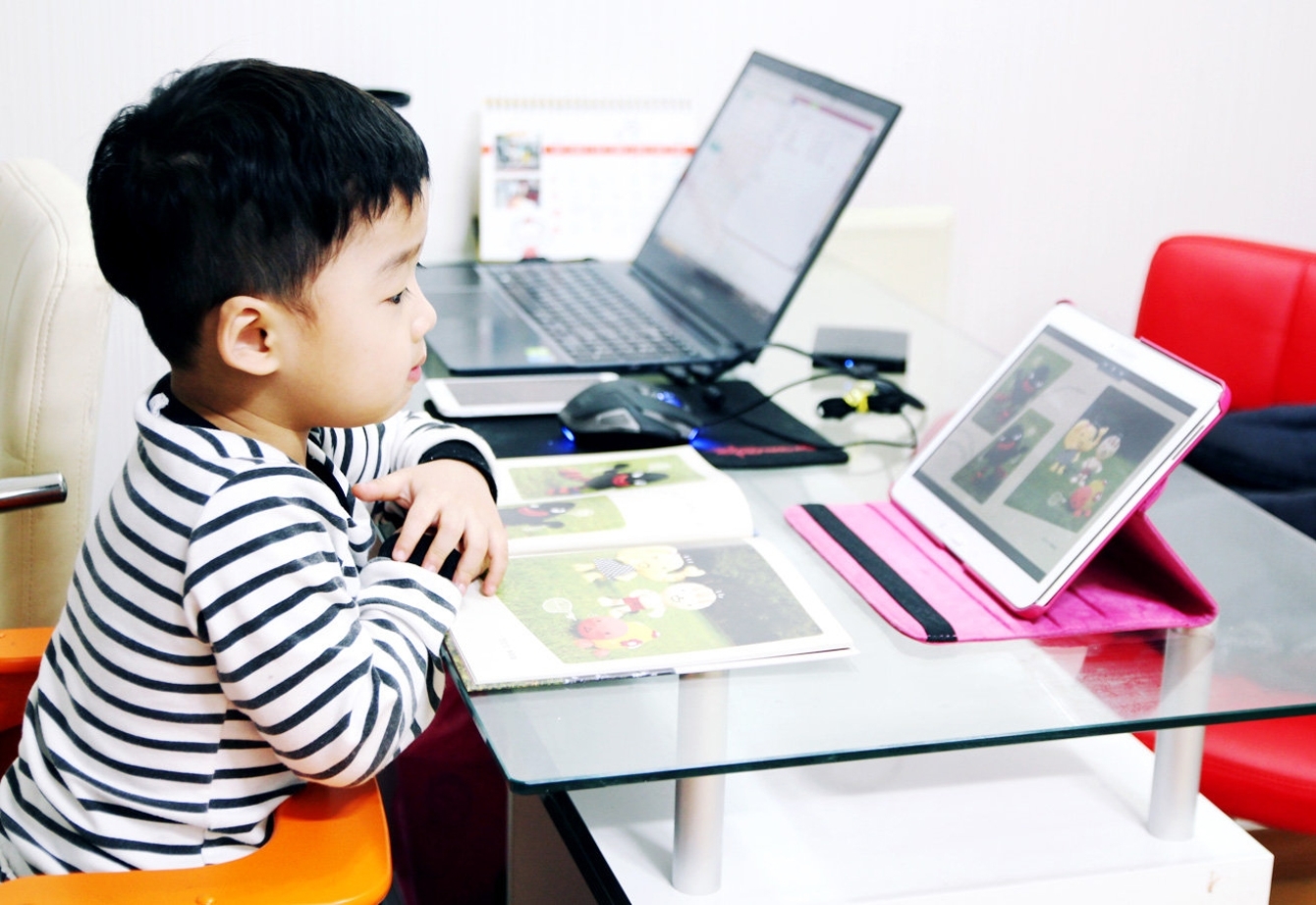 한 어린이가 교재가 놓인 책상위에 웅진북클럽 화면이 나오는 태블릿을 바라보는 모습을 보여주고 있습니다.