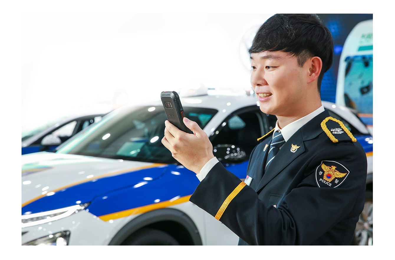 화면 중앙에 경찰차가 보이고, 화면 우측에 남자 경찰이 삼성 재난망폰 화면을 보고 있습니다.