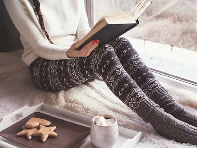니트와 겨울바지, 두꺼운 양말을 신은 여자가 바닥에 앉아 책을 보고 있습니다.