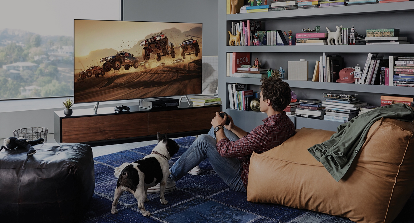 2018 QLED TV Q6F의 라이프 스타일 이미지입니다. QLED TV가 거실 테이블 위에 놓여있고, 한 남자가 QLED TV로 게임을 하고 있습니다. 