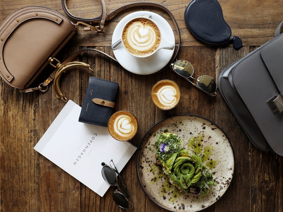 Isabelle Cheng이 찍은 음식 사진입니다. 커피, 파스타, 지갑, 선글라스, 가방 등이 나무 테이블에 있습니다.