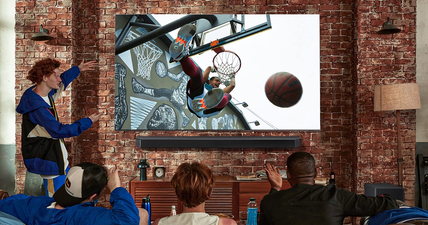 거실에서 친구들과 TV로 스포츠 경기를 즐기는 모습입니다. QLED 8K와 사운드바가 함께 보이고 화면에는 덩크 장면이 나오고 있습니다.