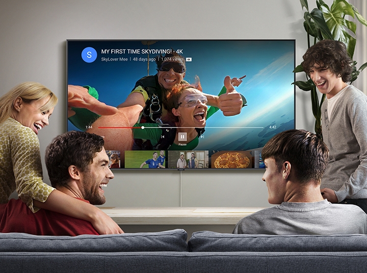 4명이 거실에서 삼성 스마트TV를 통해 고품질의 유튜브 영상을 보고 있습니다. 4K 로고가 새겨진 스카이 다이빙 영상이 스마트TV 유튜브 앱을 통해 스트리밍되고 있습니다.