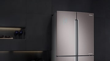하단 좌측 이미지: 블랙 톤의 주방에 측면과 정면이 보이도록 살짝 틀어진 냉장고의 상단 모습이 보입니다. 측면까지 메탈을 적용해 고급스러우며, 패밀리허브의 화면에 현재 시간을 알려주는 시계와 먹음직스러운 음식 사진이 실행되어 있습니다.