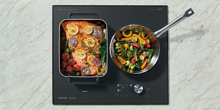 대리석으로 된 조리대 위에 전기레인지가 빌트인 방식으로 설치되어 있으며 이를 위에서 정면으로 내려다본 모습입니다. 전기레인지의 왼쪽 플렉스존에는 연어 스테이크, 오른쪽에는 야채를 볶고 있는 모습입니다.