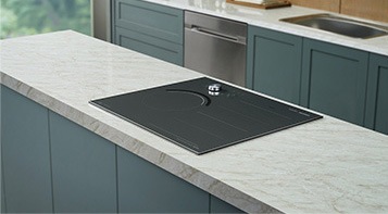 대리석으로 된 조리대 위에 전기레인지가 빌트인 방식으로 설치된 모습입니다. 뒤로 주방 용품과 싱크대가 보입니다.