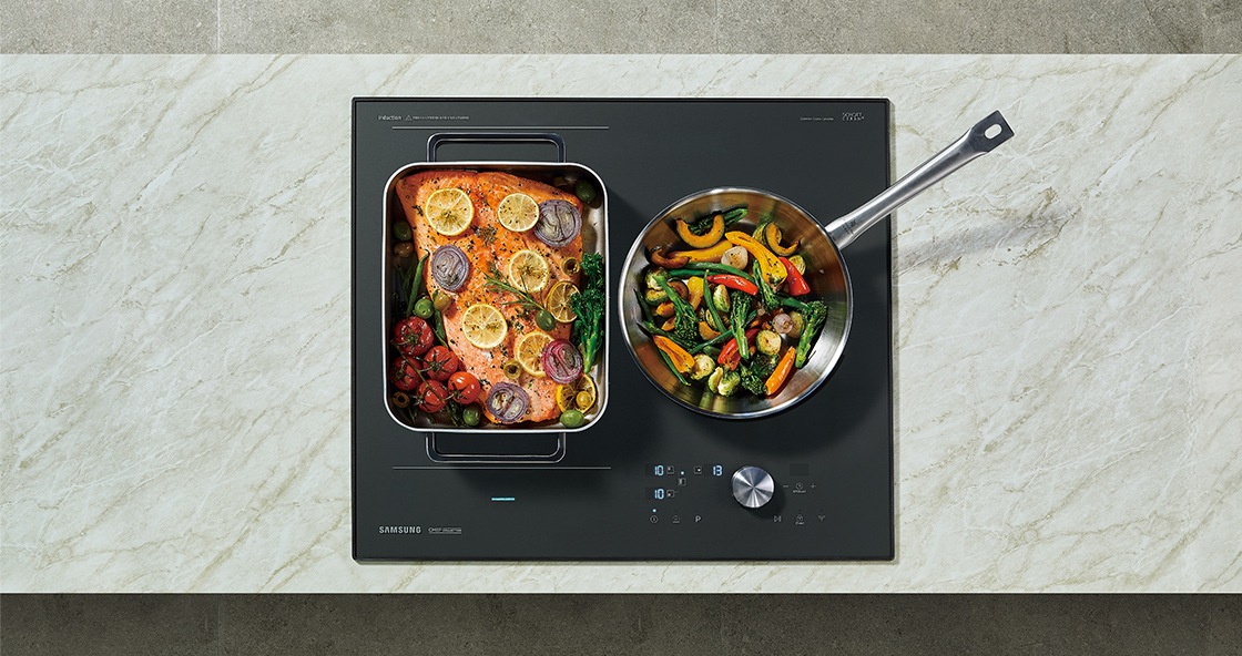 대리석으로 된 조리대 위에 전기레인지가 빌트인 방식으로 설치되어 있으며 이를 위에서 정면으로 내려다본 모습입니다. 전기레인지의 왼쪽 플렉스존에는 연어 스테이크, 오른쪽에는 야채를 볶고 있는 모습입니다.