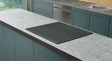 대리석으로 된 조리대 위에 전기레인지가 빌트인 방식으로 설치된 모습입니다. 뒤로 주방 용품과 싱크대가 보입니다.