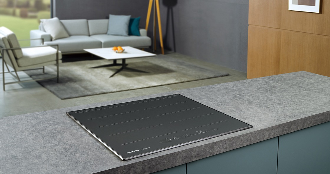 대리석으로 된 조리대 위에 전기레인지가 빌트인 방식으로 설치되어 있으며 뒤로 보이는 거실에는 밝은색의 소파와 사각테이블이 놓여 있습니다.