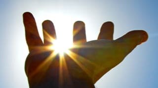 一只手伸向天空，透过指缝看到太阳。