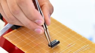Tweezers being used to assemble a practice semiconductor.