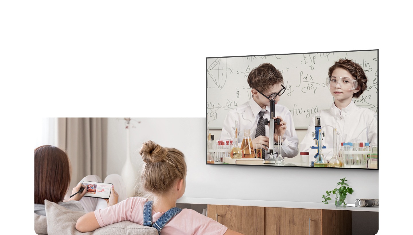 A girl and her mother are sitting on a sofa in front of the TV. The girl is watching a educational show on TV while her mother is doing something else on her Galaxy smartphone..